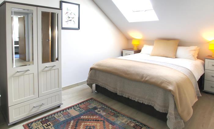 Inviting double bedroom with soft beige tones, mirrored wardrobe, and natural light from the skylight.